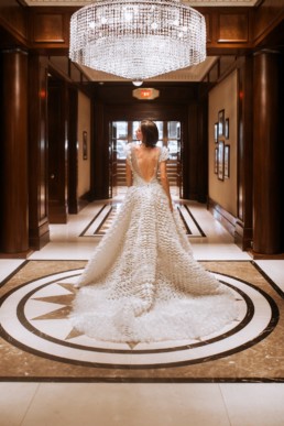 mariée de dos dans le hall de l'hôtel de luxe avec lustre en cristal, à new york. robe de mariage gemy maalouf