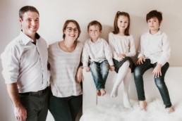 photo de famille à lattes, trois enfants assis deux parents debout. Jeans et chemises blanches