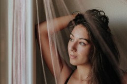 photo d'une femme qui joue avec les rideaux devant sa fenêtre. Brune aux yeux verts