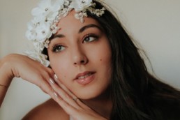 portrait d'une femme brune appuyé sur ses mains de côté. Fleurs blanches dans les cheveux