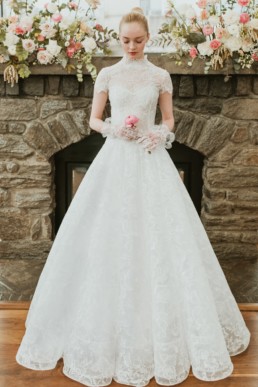 robe de mariée blanche classique et sophistiquée en dentelle, avec gants de mariage et fleurs rose dans les main. Défile de robes isabelle armstrong new york