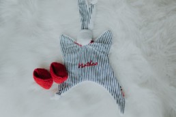 doudou et chaussons rouge tricote a la main posé sur le lit, pour futur bébé mathéo