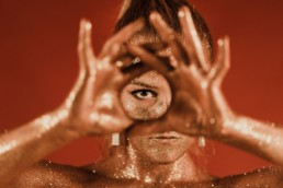 femme recouverte de paillette en or formant un cercle avec ses mains et son oeil est dans le cercle