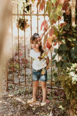 petite fille contre une grille de jardin, entourée de feuille d'automne à avignon