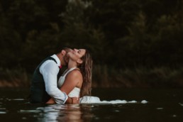 comme qui embrasse sa femme dans le coup pendant la séance photo couple après le mariage à agde. couple de mariés dans l'eau, robe de mariage qui flotte