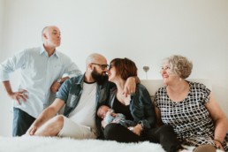 photo d'un bébé dans les bras de ses parents qui s'embrassent, et des grands parents qui souris