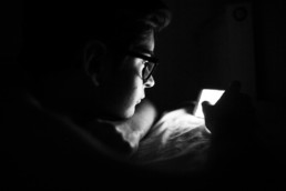 adolescent avec des lunettes, qui regarde son téléphone dans le noir. portrait en noir et blanc à montpellier