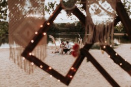 couple de mariée à leur table de mariage sur le sable. mariage en octobre. décotain de mariage avec cadre photo et macramé. Herbe de pampa, mariage bohème, vintage, champêtre et sauvage. Plus belle photo de mariage du monde