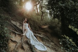 mariée assise par terre dans la forêt, robe de mariage en soie légère plaqué sur les racines des arbres. robe de mariée à bustier