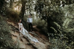 couple de mariés dans la foret assise par terre. robe bustier, homme chemise et bretelle