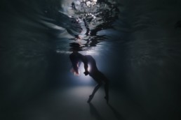 Femme qui remonte à la surface de l'eau les bras en arrière pour des portraits aquatiques à Montpellier