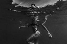 photo en noir et blanc sous l'eau d'une femme à la plage dans du grand travers à la grande motte. Le corps dans l'eau la tête à l'extérieur de l'eau. maillot de bain 2 pièces, bikini banana moon