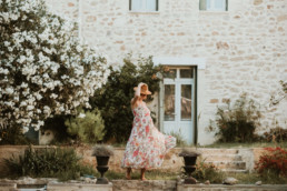 femme enceinte en robe longue a fleur, qui danse dans son jardin à Montpellier Odysseum, avec un chapeau de paille sur la tête. Meilleure photographe de Montpellier, Juvignac, Mauguio, Saint-Aunes et vendargues