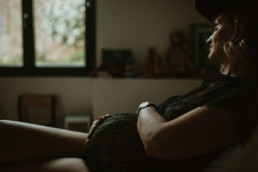 Femme enceinte qui caresse son ventre rond avec le bébé qui bouge in utero. femme assise dans la chambre du futur bébé, en body de grossesse noir a dentelle à Montpellier