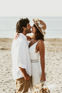couple de marié sur la plage a montpellier pour un day after sur le sable et dans l'eau. mariée avec un chapeau et bouquet bohème